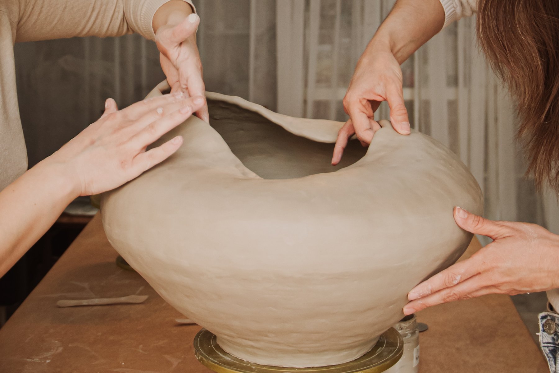 Four hands shaping a large organic ceramic vessel together on a turntable