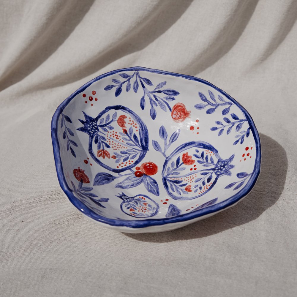 A hand-painted bowl with cobalt-and-red pomegranate motifs on draped linen