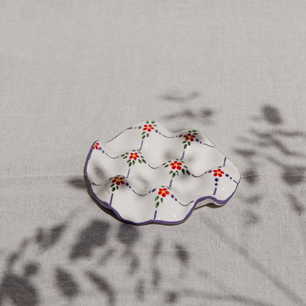 A scalloped ceramic plate with hand-painted red flowers and trailing leaves