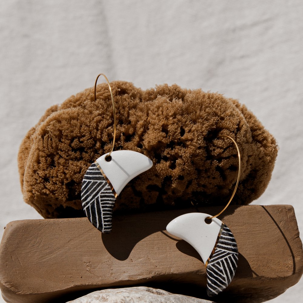 Black-and-white striped crescent ceramic earrings on a natural sea sponge