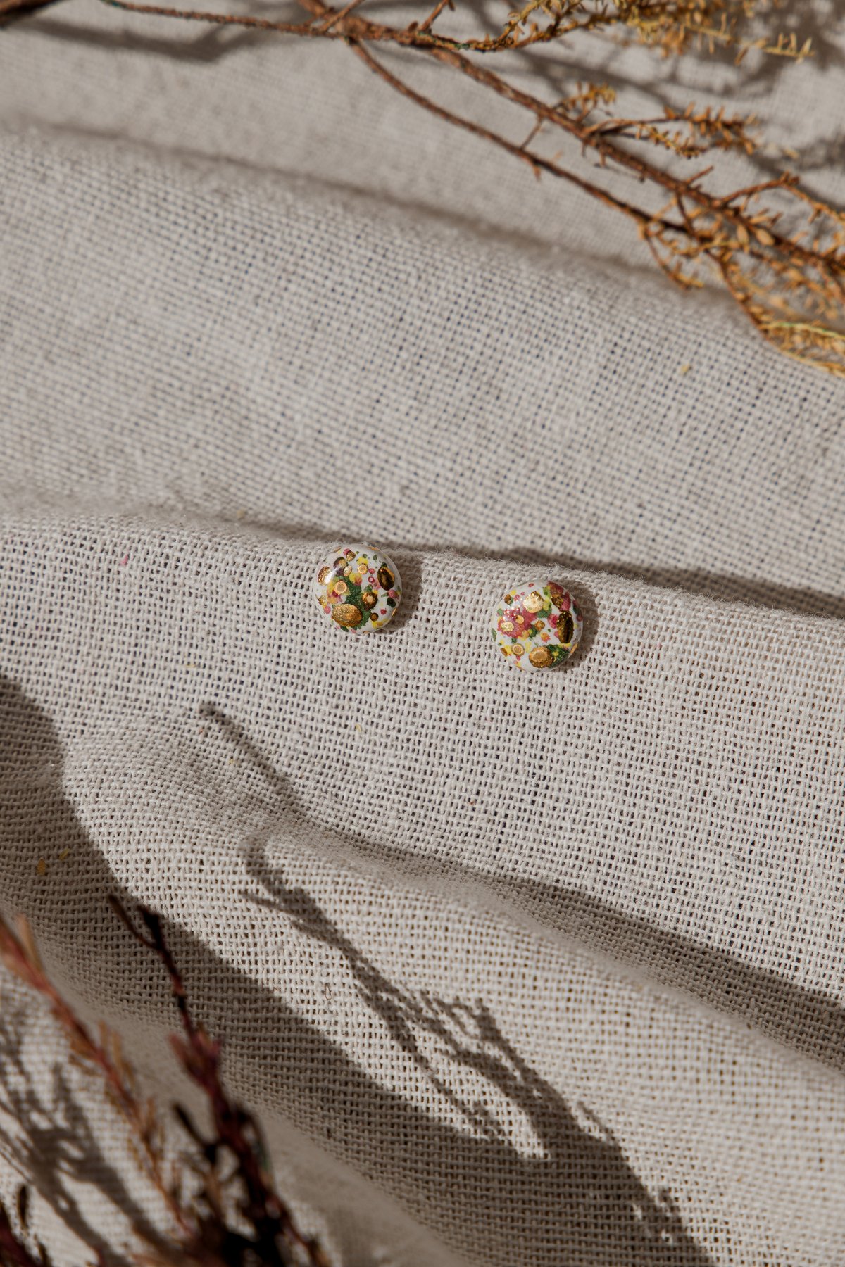 The Fragment Studs &mdash; a pair of small clay stud earrings on linen