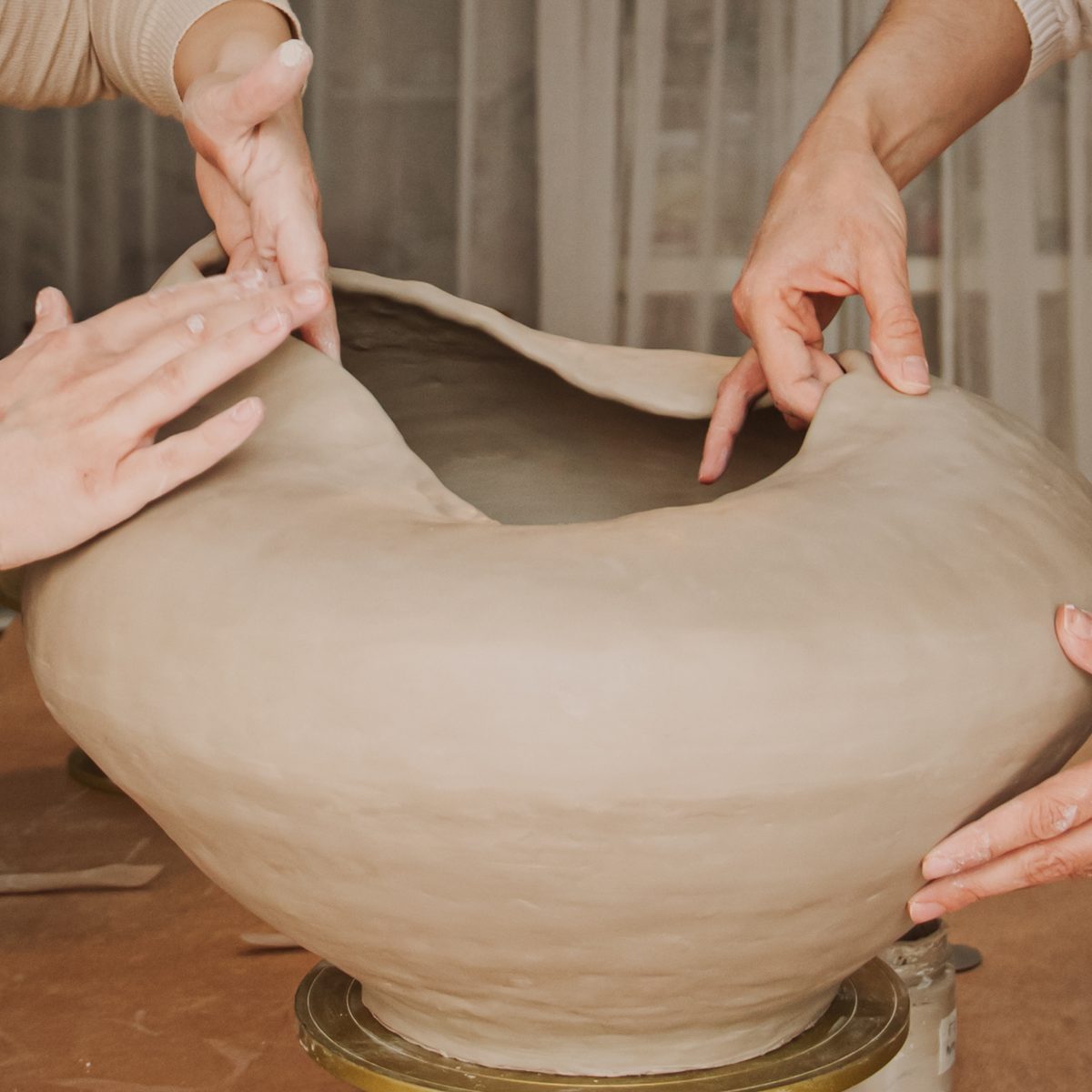 Four hands shaping a large organic ceramic vessel together on a turntable