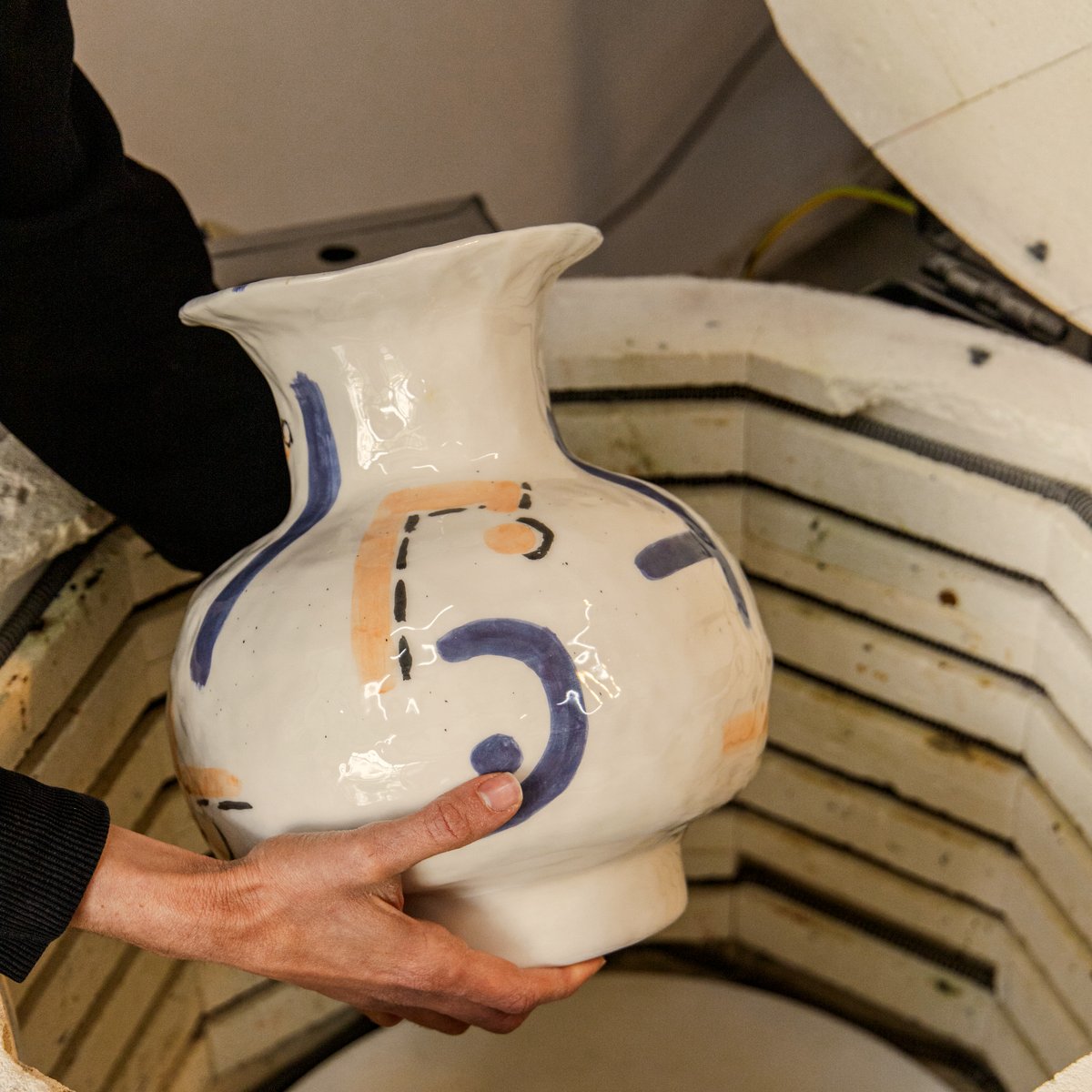 A glazed cobalt-and-ochre vase being lowered into the kiln for the high fire